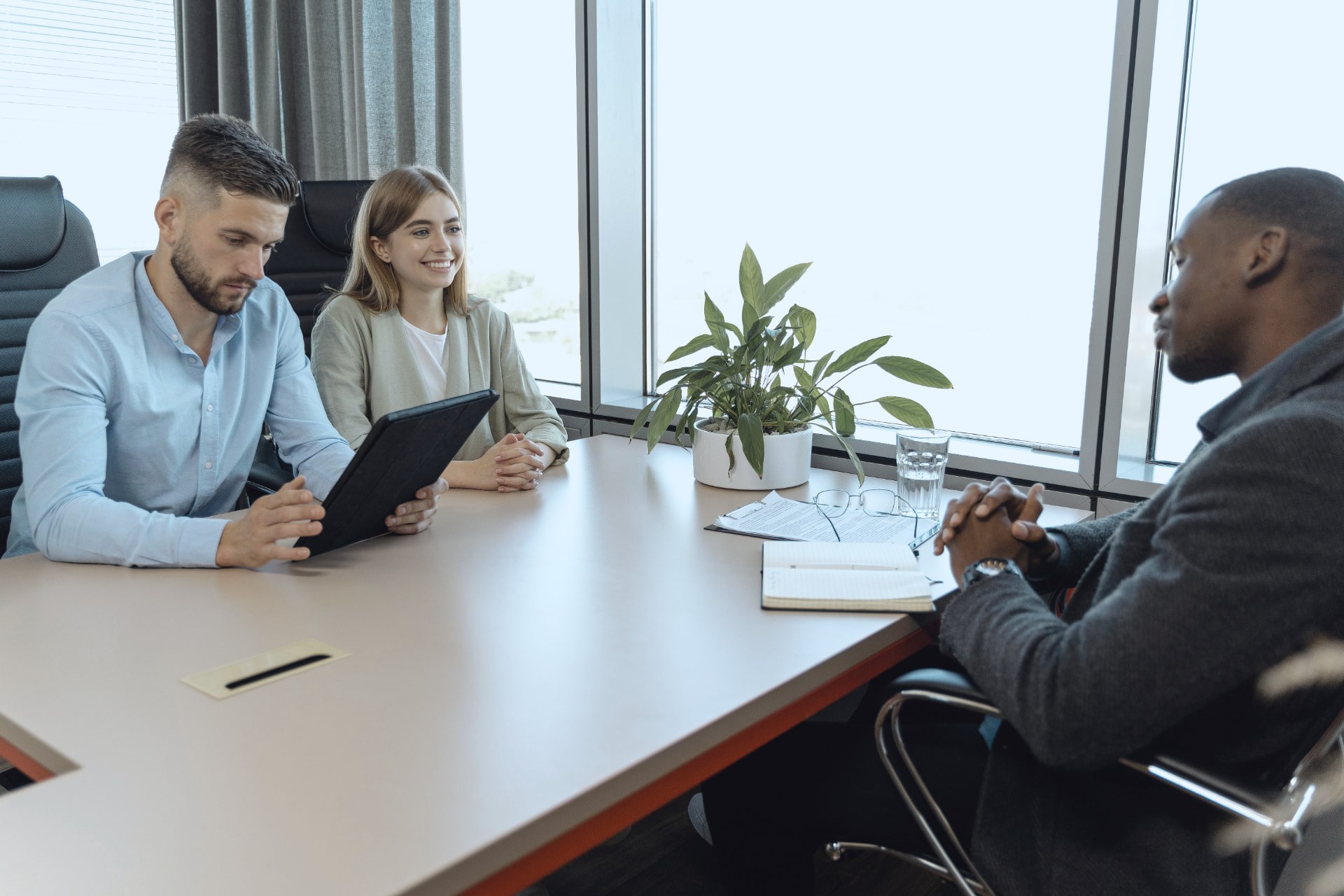 Candidates meeting two interviewers across a table in a glass-walled office with a city view