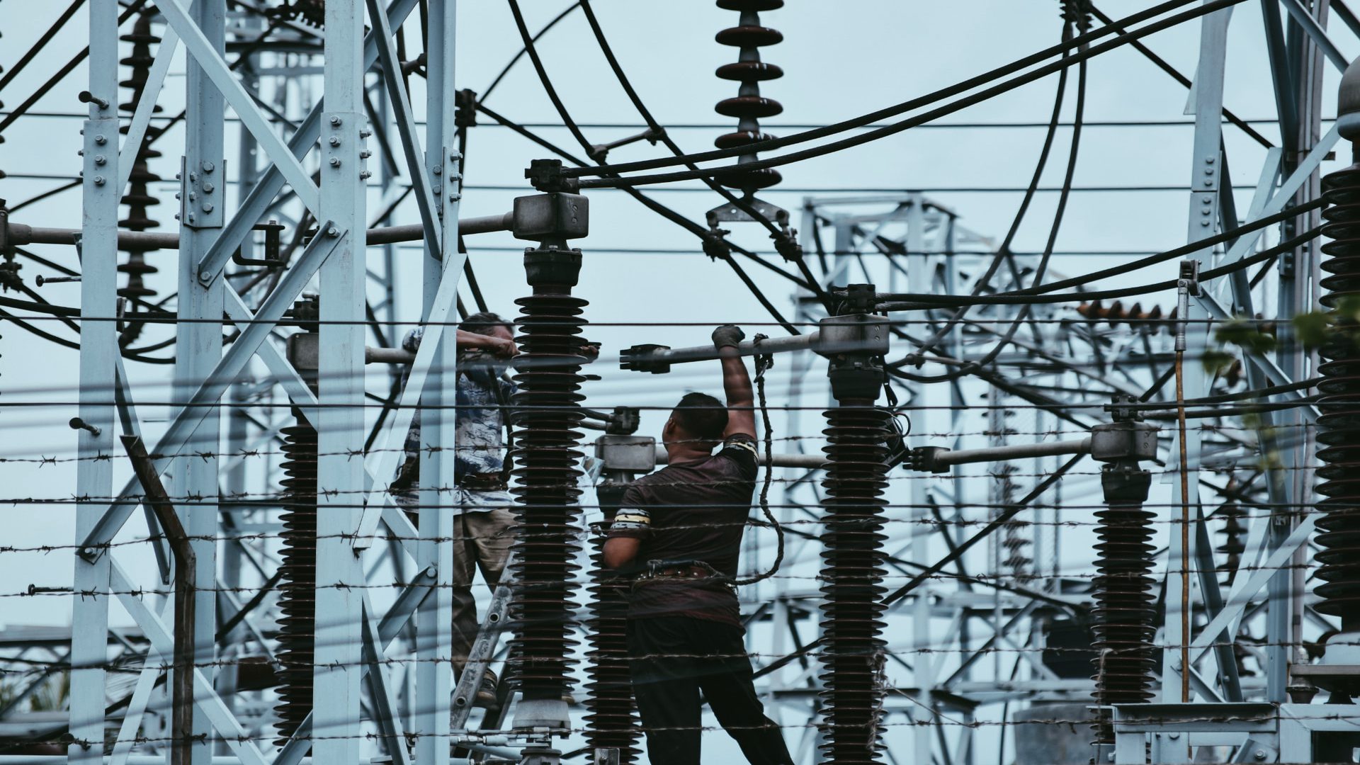 Technicians working on high-voltage insulators and busbars inside a substation