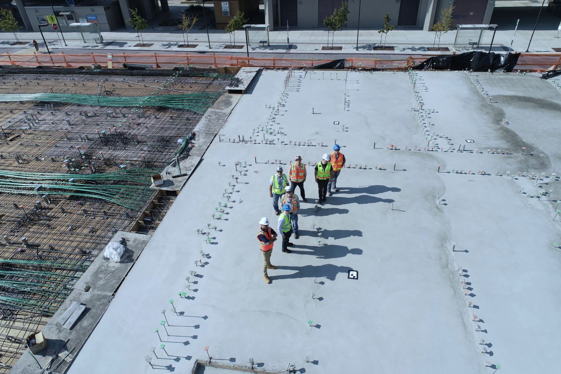 Overhead view of a site team on a poured slab beside unpoured rebar foundations